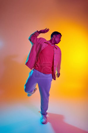 Stilvoller afrikanisch-amerikanischer Mann in trendiger Kleidung mit lebendigem Farbverlauf Hintergrund, dynamische Pose