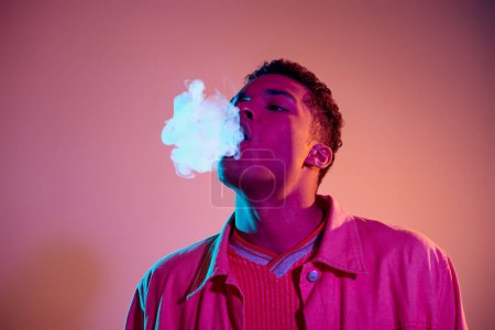 portrait of african american man exhaling smoke against vibrant background with blue lighting, vape