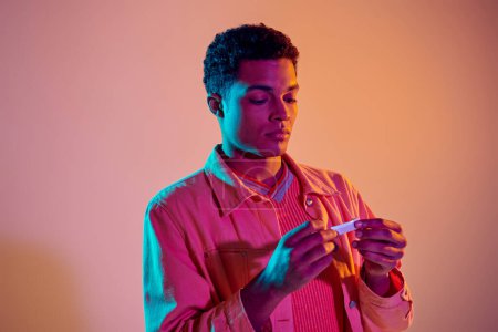 Afrikanischer Amerikaner dreht Zigarette zum Rauchen auf buntem Hintergrund mit blauer Neonbeleuchtung