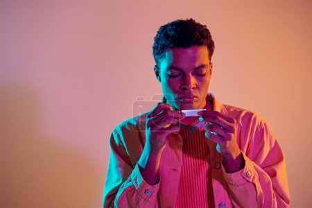 Afroamerikaner dreht Zigarette zum Rauchen auf buntem Hintergrund mit blauer Neonbeleuchtung
