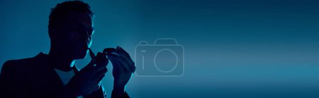 Foto de Pancarta, hombre afroamericano sosteniendo más ligero mientras fuma pipa sobre fondo azul oscuro con iluminación - Imagen libre de derechos