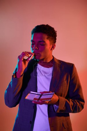 handsome african american man holding cigarette case on pink background with blue lighting