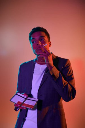 portrait of curly african american man holding cigarette case on pink background with blue lighting