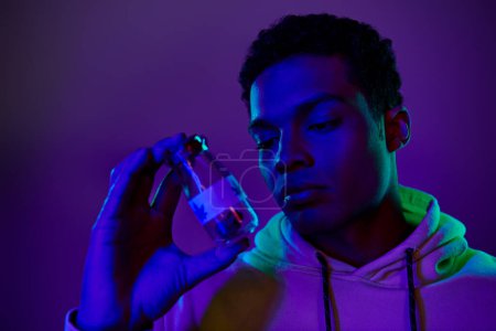 portrait of african american man in hoodie holding jar with medical cannabis on dark blue background
