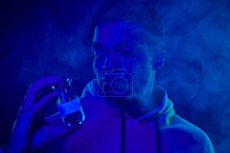 portrait of african american man in hoodie holding jar with medical cannabis on dark blue background