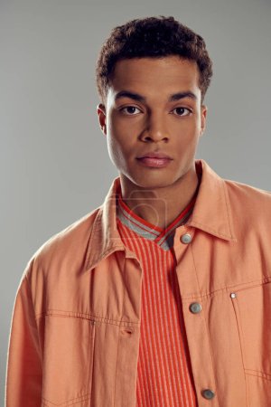 junger afrikanisch-amerikanischer Mann in pfirsichfarbenem Hemd schaut in die Kamera vor grauem Hintergrund, Gen z fashion