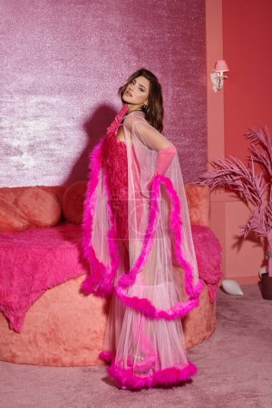 glamouröse junge Frau in rosafarbenem Federkleid und Handschuhen posiert in einem luxuriösen Rahmen