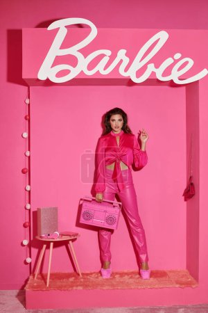 Téléchargez les photos : KYIV, UKRAINE - 14 JUILLET 2023 : jolie jeune femme aux cheveux bouclés debout en tenue rose et tenant boombox près de Barbie signe - en image libre de droit