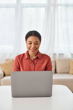 satisfied african american nutritionist using laptop while working remotely from her kitchen