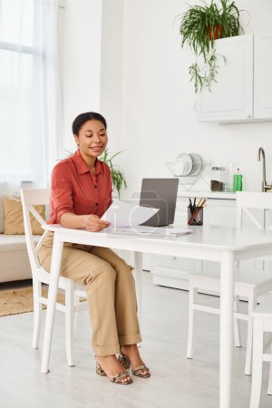 happy african american nutritionist reviewing documents near laptop for online consultation at home