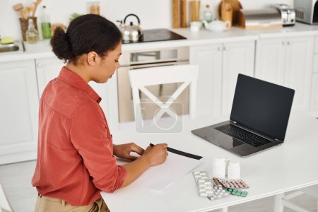nutritionist writing prescription near different medication next to laptop with blank screen