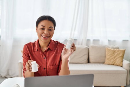 positive nutritionist showing bottles with different medication during online consultation on laptop