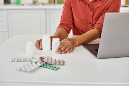 cropped view of african american dietitian near bottles with different medication on table