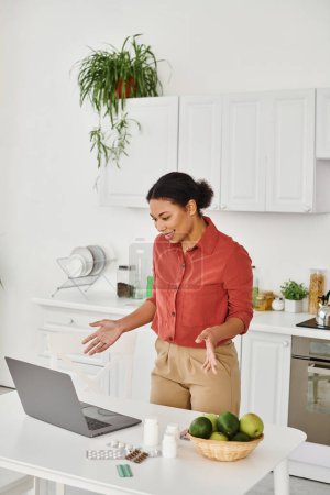 Foto de Nutricionista afroamericano gesto mientras está de pie cerca de la computadora portátil y ofrece consejos de dieta en línea - Imagen libre de derechos