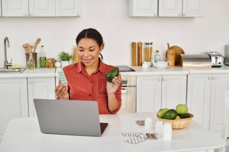 african american nutritionist holding avocado and supplements while giving diet advice from laptop