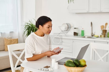 happy african american nutritionist with pills looking at laptop during an online consultation