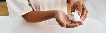dietista afroamericano recortado verter píldoras en la palma de la mano de la botella de medicamentos, pancarta