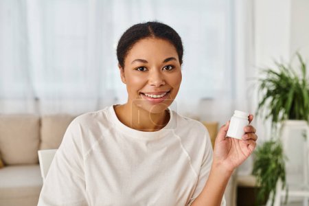 portrait of happy african american nutritionist holding supplements in a bottle for healthy diet