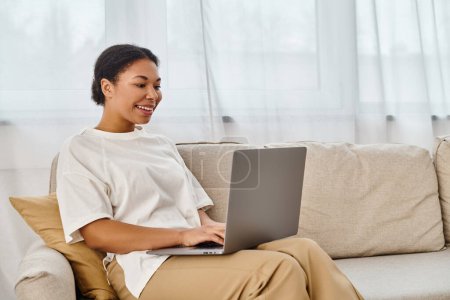happy african american nutritionist using laptop while working from home in living room