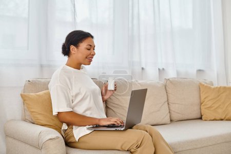 happy african american nutritionist with supplements giving dietary tip via laptop in living room