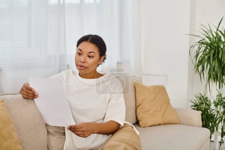 brünette afrikanisch-amerikanische Frau in lässiger Kleidung liest Diätrezepte und entspannt sich auf dem Sofa
