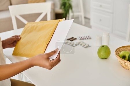 zugeschnittene Ansicht einer schwarzen Frau, die ihren Ernährungsplan überprüft, während sie den Umschlag in der Nähe von Nahrungsergänzungsmitteln öffnet