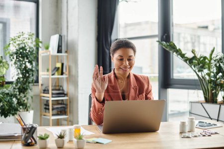 Photo for Happy african american nutritionist waving hand at laptop from her plant-filled office space - Royalty Free Image