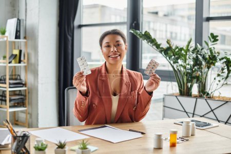 joyful african american nutritionist showing different medication while sitting in her office