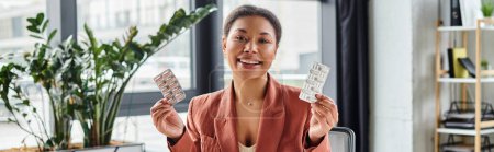 joyful african american nutritionist showing different medication while sitting in office, banner