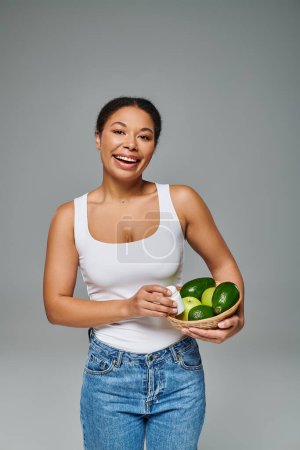 diététiste afro-américaine joyeuse avec des fruits verts et des suppléments présentant un mode de vie sain