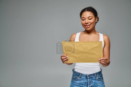 happy african american dietitian holding envelope containing a dietary plan on grey backdrop