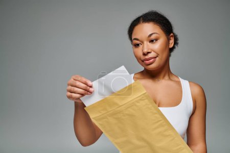 fröhlich afrikanisch-amerikanische Diätassistentin hält Umschlag mit Ernährungsplan vor grauem Hintergrund