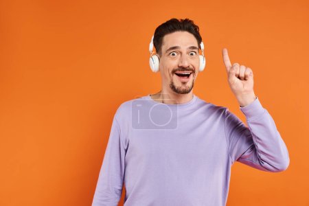 erstaunt bärtiger Mann mit drahtlosen Kopfhörern, Musik auf orangefarbenem Hintergrund hörend, Idee Geste