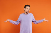 confused bearded man in purple sweater showing shrug gesture with his hands on orange background tote bag #692775624