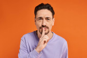 bearded man holding finger near lips while showing hush sign on orange background, silence Longsleeve T-shirt #692775662