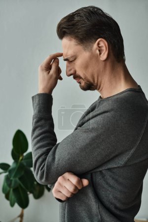 gestresster und bärtiger Mann mit geschlossenen Augen, der zu Hause unter Kopfschmerzen, Migräne und Stirnrunzeln leidet