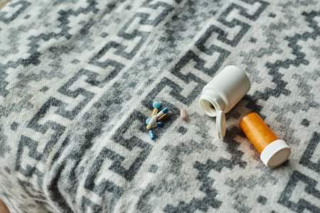 Foto de Diferentes medicamentos en manta gris con adorno, pastillas cerca de botellas de medicamentos de plástico - Imagen libre de derechos