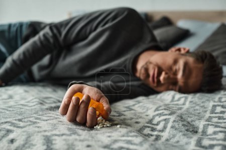 blurred shot of bearded man sleeping on bed near bottle with medication,
