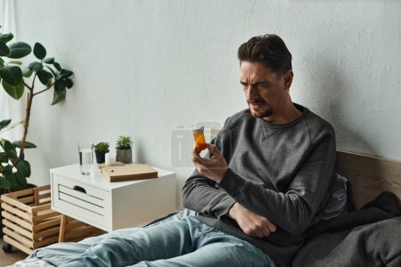 Nachdenklicher bärtiger Mann untersucht Flasche mit Tabletten, während er im Schlafzimmer auf dem Bett sitzt, Behandlungsplan