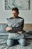 bearded man feeling discomfort and holding pillow while sitting on bed at home, troubled patient puzzle #692778254