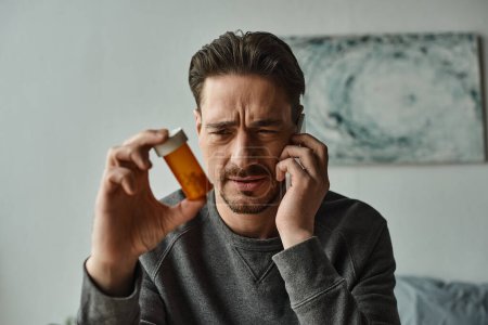 Besorgter bärtiger Mann spricht auf Smartphone, während er sich Medikamente anschaut, Online-Beratung