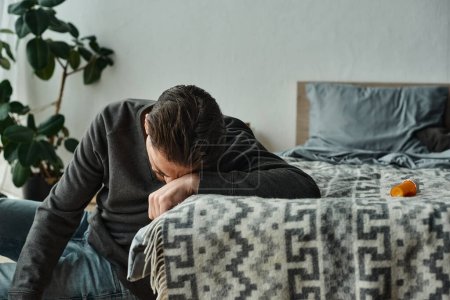 bärtiger Mann leidet unter Schmerzen und lehnt auf grauer Decke auf dem Bett im modernen Schlafzimmer, Schmerzen