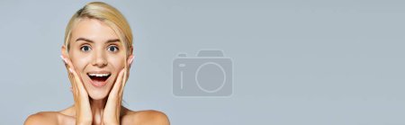 horizontal view of pretty girl with blonde hair and gray eyes posing surprise in gray background