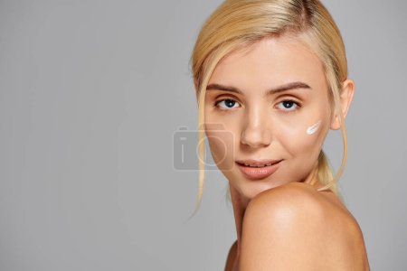 portrait woman face with radiant skin and lotion on her cheek looking playful in grey background