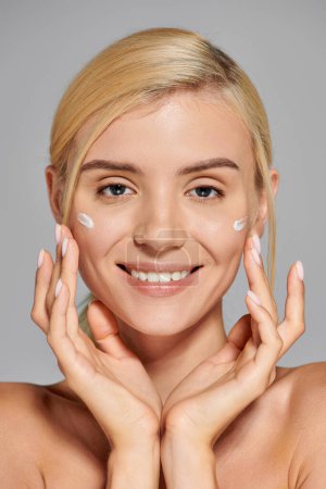 Photo for Portrait smiling young woman with hands around her face and cream on cheeks against gray background - Royalty Free Image
