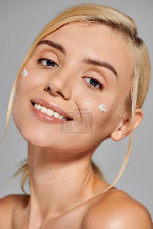 smiling pretty girl with healthy skin and lotion on her cheeks against gray background