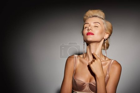 beautiful blonde girl with red lips and long earrings posing against grey background