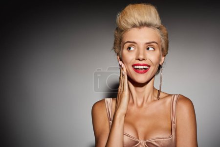 Téléchargez les photos : Blonde jeune femme avec rouge à lèvres posant et regardant de côté en arrière-plan gris - en image libre de droit