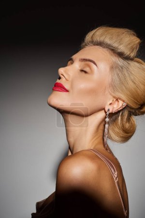 charming girl in her 20s with red lips closing her eyes with pleasure against grey background