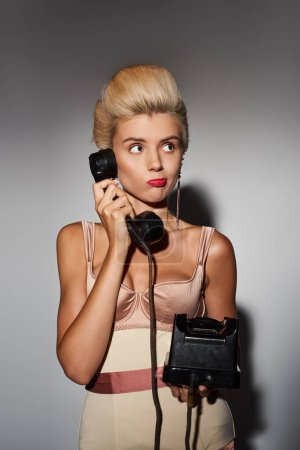 Charmante junge Frau mit rotem Lippenstift verwirrt Gespräch auf Retro-Telefon in grauem Hintergrund